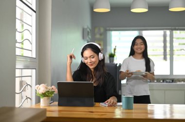 Annesi tablet bilgisayarda çalışırken küçük kız annesi için fırın hizmeti veriyor..