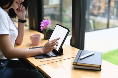 Güzel bir kadın ahşap tezgahta otururken beyaz ekranlı bir tablet kullanıyor..