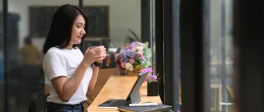 Güzel bir kadın, ahşap tezgahta otururken bir kahveyle rahatlıyor..