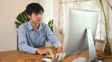 Akıllı bir adam, rahat bir odadaki ahşap bir masaya koyan bir bilgisayar kullanıyor..