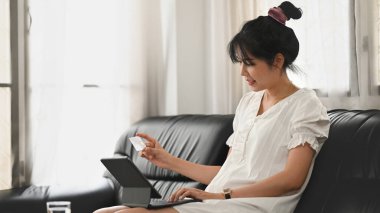 Güzel bir kadın kanepede otururken bilgisayar tableti ve kredi kartı kullanıyor..