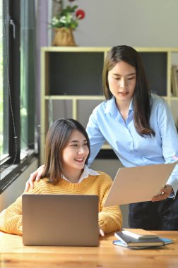 İki kadın, ahşap çalışma masasında bir bilgisayarla birlikte çalışıyorlar..