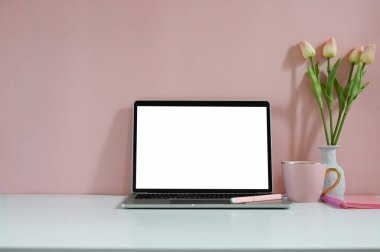 Dizüstü bilgisayar, defter, kalem ve kahve fincanlı lale çiçekleriyle pembe çalışma alanı modeli.