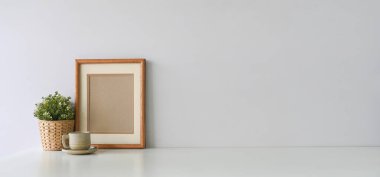 Boş fotoğraf çerçevesi, saksı çiçeği ve bardak masanın üstünde.