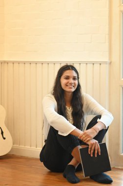 Güzel bir kadın elinde bir defter tutarken ahşap zeminde müzik okulunun dinlenme odasında arka plan olarak oturuyordu..