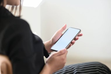 Kadının kesilmiş görüntüsü oturma odasında otururken cep telefonu kullanıyor..
