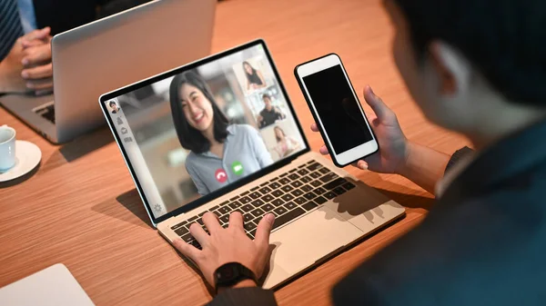 businessman meeting with team in conference video call on laptop and holding smartphone with blank screen