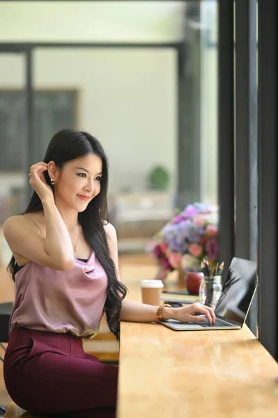 Young Asian woman is working with a black blank screen computer laptop at the wooden counter.