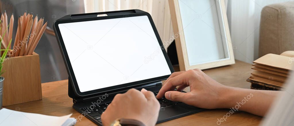 A cropped image of hands is using a computer tablet at the wooden working desk.