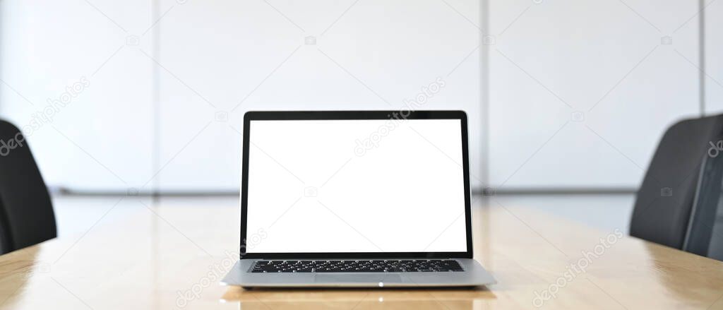 A computer laptop with a white blank screen is putting on a table in the conference room.