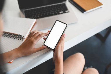 Bir kadının kırpılmış görüntüsü çalışan beyaz masadaki akıllı telefonu kullanıyor..