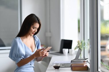 Güzel bir kadın modern ofiste cep telefonu kullanıyor..