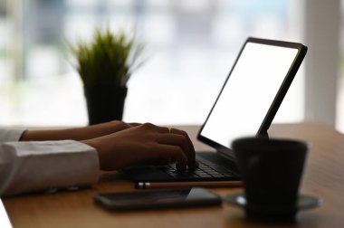 Ahşap masa üzerindeki tabletle işine odaklanan kadın girişimcinin yan görünüşü.