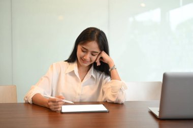 Genç kadın elinde stilus kalemle dijital tablet hakkında bilgi tutuyor..