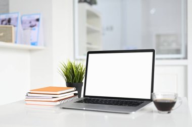 Çalışma alanının boş ekranlı görüntüsü ve bulanık ofis odası arka planına sahip beyaz masadaki kahve fincanı..