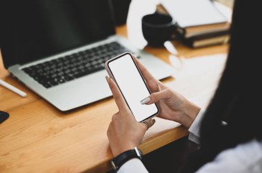 Ahşap ofis masasında beyaz ekranlı akıllı telefon tutan kadın..