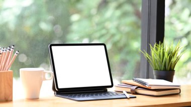 Akıllı klavye, kahve fincanı, kalemler ve çalışma masası üzerine kitap ile kesilmiş tablet görüntüsü. Grafik görüntüleme montajı için boş ekran.