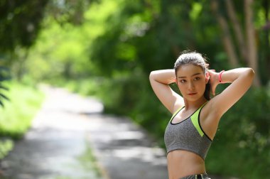 Sağlıklı genç bir kadın dışarıda ısınıyor. Kollarını uzatıyor ve başka tarafa bakıyor..