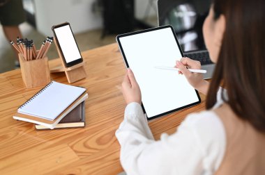 Kırpılmış çekim yapan kadın tablet bilgisayarla çalışıyor ve ahşap masada boş akıllı telefon ekranı var..