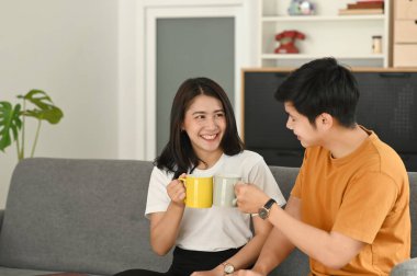 Evdeki kanepede oturup kahve içen neşeli genç çift..