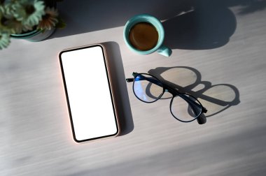 Top view of simple workplace with blank screen smart phone, glasses and coffee cup on wooden table.