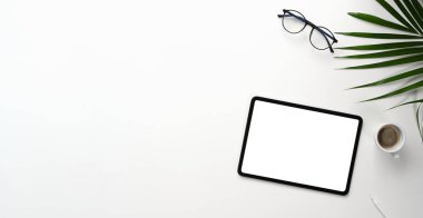 Top view of minimal workplace with blank screen tablet, glasses and coffee cup on white desk.