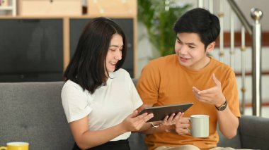 Kız arkadaşı erkek arkadaşına tablette bir şey gösteriyor ve evdeki kanepede dinleniyor..