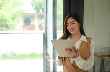 Genç Asyalı grafik tasarımcısı, tahta masadaki boş ekranla bilgisayar tableti üzerinde çalışıyor..