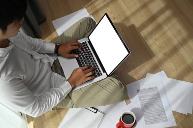 Genç adam evde oturmuş kahve içiyor ve beyaz ekranlı dizüstü bilgisayar kullanıyor..