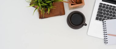 Top view of white office desk with coffee, laptop and notebook. 