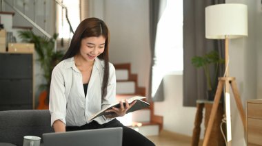 Güzel beyaz bir kadın kanepede dinleniyor ve evde kitap okuyor.. 