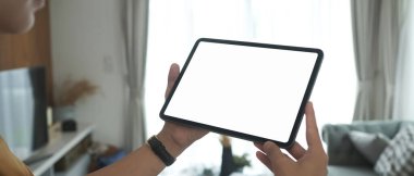 Cropped shot of man hands holding tablet with white screen in living room at home.