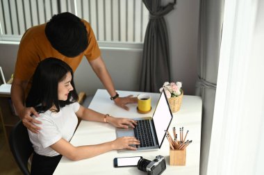 Evdeki oturma odasında dizüstü bilgisayarda internette gezinen genç çift..