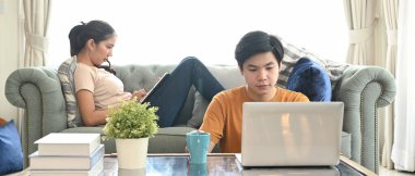 Genç çift yaşam odasında web sörfü yapmak için dijital tablet ve laptop kullanıyor..