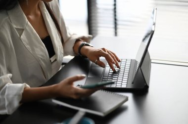 Cropped shot of businesswoman working on mock up tablet while using smart phone on office desk.