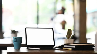 Simple workplace with blank screen computer tablet and office supplies on black wooden table.