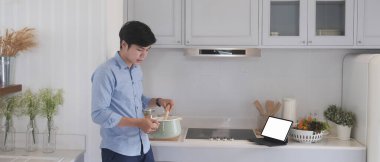 Genç adam dijital tablet kullanıyor ve mutfakta modern yemekler yapıyor..