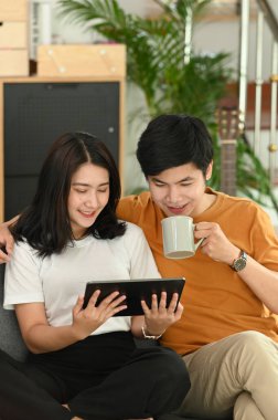 Mutlu genç çift kahve içiyor ve evdeki kanepede birlikte tablet kullanıyorlar..