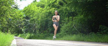 Spor elbiseli güzel genç bir bayan sabah parkta koşuyor..