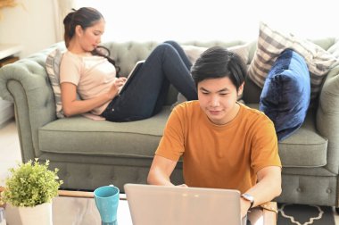 Genç çift oturma odasındayken internette sörf yapmak için laptop ve taplet kullanıyor..