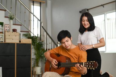Genç bir çift evdeki salonda birlikte gitar çalıyor..