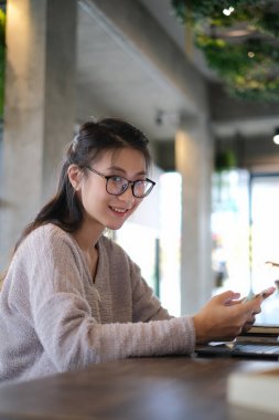 Sıradan giyinmiş genç bir kadın akıllı bir telefon kullanıyor ve Camela 'ya gülümsüyor..