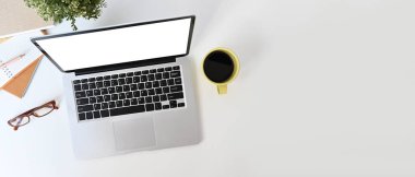 Top view of minimal workplace with blank screen laptop and office supplies on white desk.