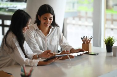 İki tasarımcı toplantı odasında beyaz masada tablet maketi ile projelerinde danışmanlık yapıyor.