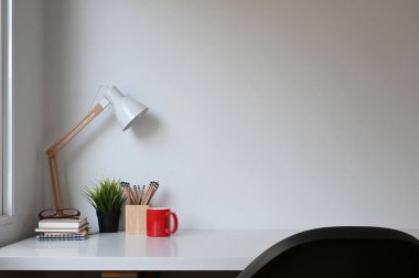 Simple workspace with lamp, plant, coffee cup and copy space on white table.