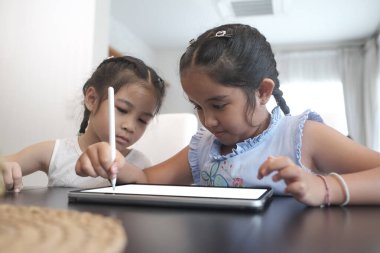 İki küçük kız oturma odasında stiluspen ile tablet ekranında birlikte resim çiziyor..