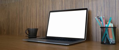 Workspace with laptop computer blank screen, coffee cup, stationery on wooden desk.