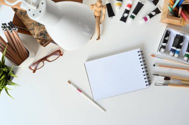 Overhead shot of designer work space with notebook and equipment on white desk.