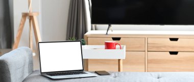 Mock up white screen laptop standing on the sofa in the cozy living room at modern home.
