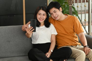 Neşeli genç çift oturma odasındaki kanepede selfie çektirsin..